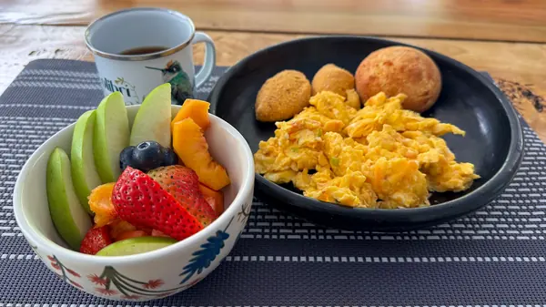 Desayuno con fruta picada, huevos revueltos, pandebonos y café