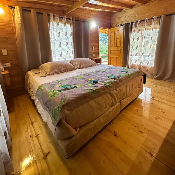 Habitación de madera con cama doble y ventanas al bosque